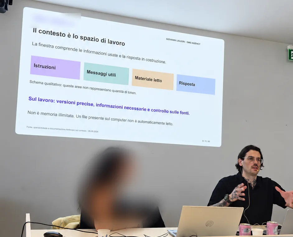 Sessione di formazione: Giovanni Liguori spiega come Claude usa il contesto, con la slide proiettata alle spalle. Il volto della persona accanto è sfocato.